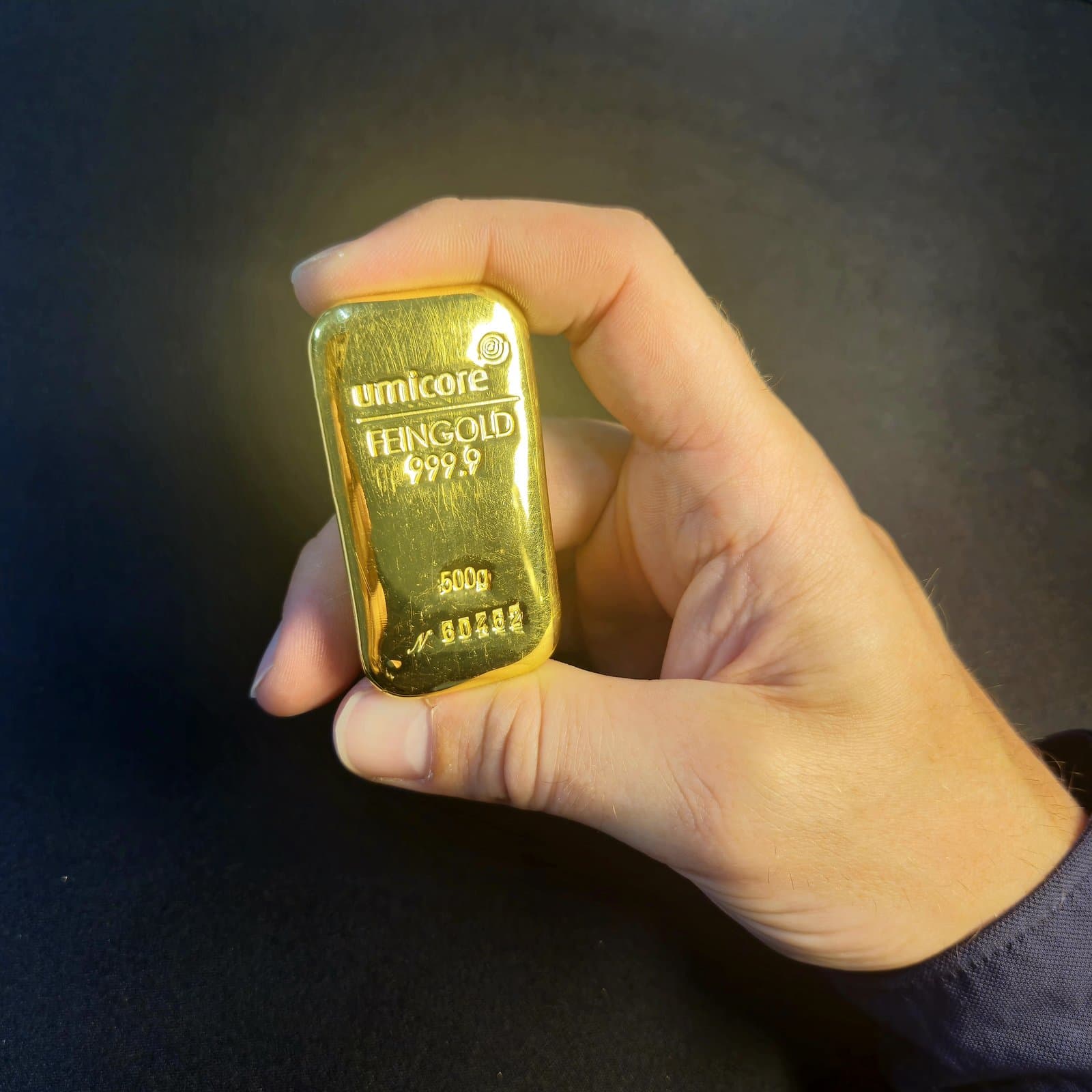 Lingot d'or Umicore 1 kg tenu en main — échelle humaine, certifié LBMA